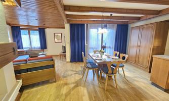 A cozy living and dining room with wooden floors and modern furniture. The large windows provide plenty of natural light and a view of the surroundings.