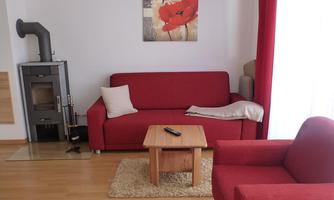 A cozy living room with red-colored sofas and a wooden table. On the wall hangs a picture with red floral motifs.