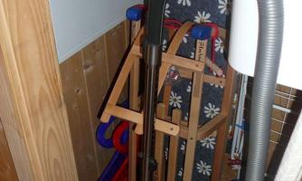 A small storage room with a vacuum cleaner, a laundry rack, and various other items. The walls are made of wood and there are some colorful items in the background.