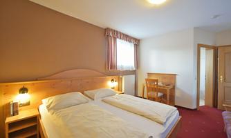 A cozy hotel room with a double bed and a table. The walls are light, and the decor is simple and modern.