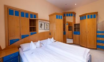 A bright bedroom with a large double bed and wooden shelves. The furniture is designed in a modern style with blue accents.