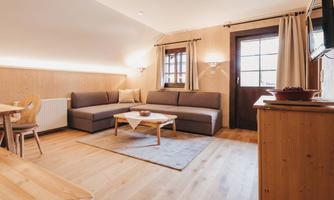 A cozy living room with a gray sofa and a wooden table. Large windows provide a view outside and ensure plenty of daylight.