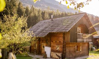 A charming wooden house in the green, surrounded by trees and mountains. The warm rays of the sun bathe the scene in golden light.