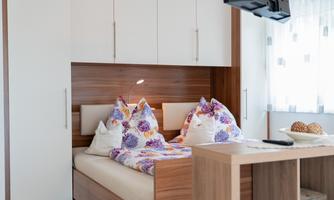 A cozy bedroom with a double bed and colorful pillows. The bright decor and the window create a friendly atmosphere.