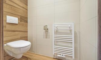 A modern bathroom with a white toilet and a towel holder. The walls are in light colors, and the floor has a wood look.