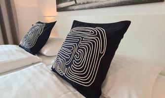 A modern bedroom with two pillows on a bed. A black-and-white photo of a landscape hangs on the wall.