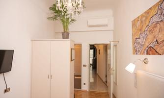 A bright room with a large wardrobe and a modern television. Above the wardrobe is a plant, and there is a piece of artwork on the wall.