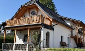 A modern house with a wooden balustrade and terrace. The garden is well-kept and the surroundings are green and inviting.