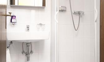 A modern bathroom with a shower and a sink. The walls are light tiled and the floor is blue.