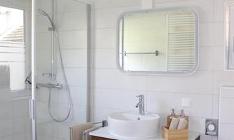A modern bathroom with a shower and a wooden sink. Bright tiles and a large mirror give the room a friendly atmosphere.