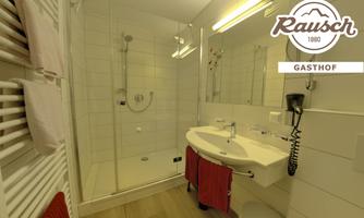 A modern bathroom with a shower and a double sink. White tiles and wooden flooring create a bright, inviting atmosphere.