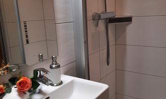 A modern bathroom with a shower and a sink. A pink flower and a towel are placed on the vanity.