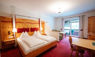 A cozy hotel room with a double bed and wooden interior. There is a small table and access to a balcony.