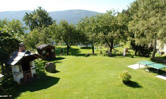 A green landscape with trees and a spacious lawn. In the background, mountains and recreational opportunities are visible.