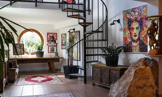 An inviting entrance area with a curved staircase and colorful artworks on the walls. Large windows let in plenty of light, while plants create a fresh atmosphere.