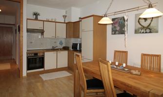 A modern kitchen with wooden cabinets and a wooden dining table. Colorful pictures adorn the walls, creating an inviting atmosphere.