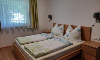 A cozy bedroom with a double bed and bright wood design. A large window with curtains lets in plenty of daylight.