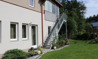 A modern house with a metal staircase and a well-kept garden. The surroundings are green and invite relaxation.