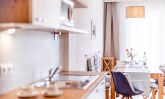 A modern kitchen with a dining area. The room is bright and warmly decorated, with natural light streaming through the windows.