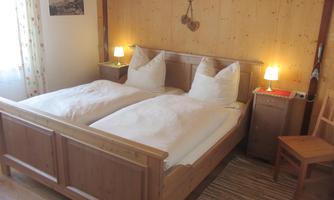A cozy bedroom with a large double bed and two nightstands. The walls are made of wood, and soft light creates an inviting atmosphere.