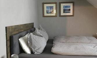 A modern bedroom with a large bed and checkered pillows. Two pictures hang on the wall, and there is a small lamp next to the bed.