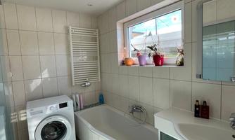 A modern bathroom with a bathtub and a washing machine. It has bright tiles and a window that lets in daylight.