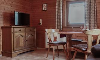 A cozy room with wooden walls and a television. There is a dining table with chairs and a sideboard.