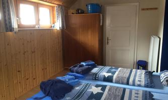 A simple bedroom with two beds and blue bedding. The room has wooden paneling, a wardrobe, and windows with curtains.