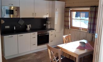 A modern kitchen with white cabinets and a stove. A dining table with two chairs and a view of the window.