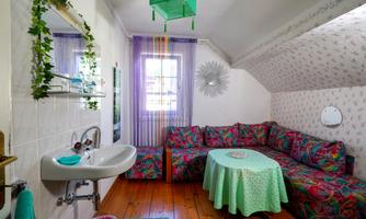 A cozy room with a colorful couch and a round table. The walls are light and decorated with a floral pattern.