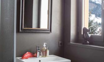 A modern bathroom with a white sink and a wooden frame. A large mirror reflects the light from a window overlooking the mountains.