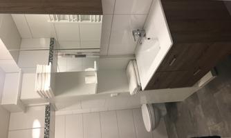 A modern bathroom with a sink and wooden cabinets. The walls are tiled in light colors and there are towels on a shelf.