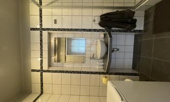 A modern bathroom with white tiles and a sink on a black table. A shower area with glass partition is also present.