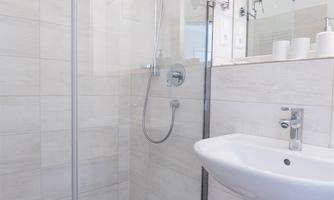 A modern bathroom with a glass shower and a sink. The floor is designed with pretty, small tiles.