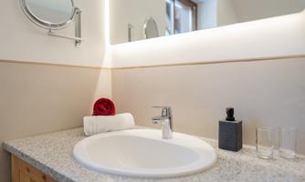 A modern bathroom with a sink and a large mirror. Towels and toiletries are neatly arranged.