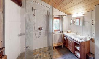A modern bathroom with a shower cabin and a bathtub. There are wooden furniture and large windows that let in natural light.