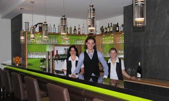 A modern bar with a bright counter area. Three staff members are smiling behind the counter.
