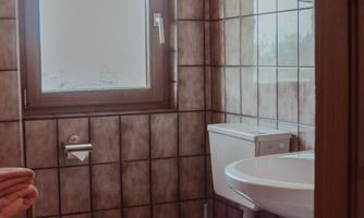 A small bathroom with brown tiles. There is a sink, a toilet, and towels in orange.