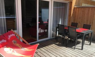 A cozy terrace with a dining table and chairs. In the foreground, there is a lounger with a red cover.