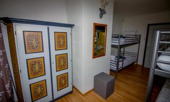 A simple dormitory with bunk beds and a decorative wardrobe. The floor is made of wood and the room feels bright and inviting.