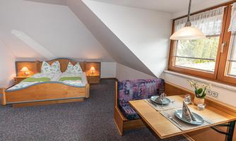 A cozy bedroom with a double bed and a view of a window. A dining table with dishes and a flower decoration complements the room.