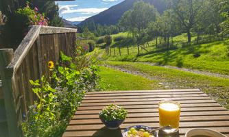 A cozy table on a terrace with fresh fruits and drinks. In the background, a green landscape with hills and trees.
