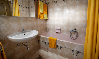 A bathroom with a bathtub and a sink. The walls are decorated with light tiles and yellow towels.