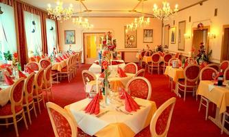An elegant restaurant with white-clothed tables and red chairs. The walls are adorned with artwork and large windows provide plenty of light.