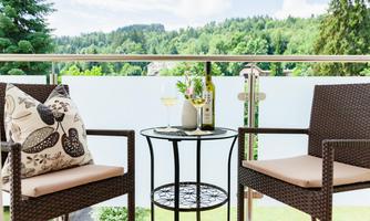 A relaxing balcony with two chairs and a small table. On the table are wine and a decorative plant, overlooking a green landscape.