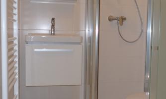 A modern bathroom with a shower and a sink. The walls are brightly tiled and there is a large mirror.