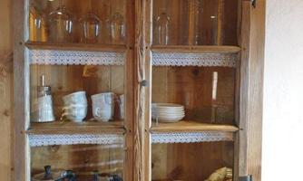 A wooden cupboard with glasses and dishes. Some cups and a coffee pot are visible.