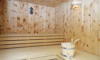 A cozy sauna with wooden paneling and benches. A wooden container is ready for water.