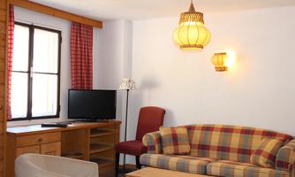 A cozy living room with a checked sofa and a television. The walls are painted light and there is warm lighting.