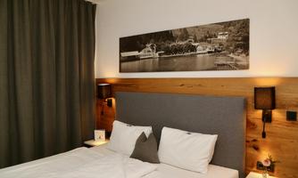 A cozy bedroom with a double bed and a modern wooden frame. A picture of a landscape hangs on the wall, and the curtains are dark gray.